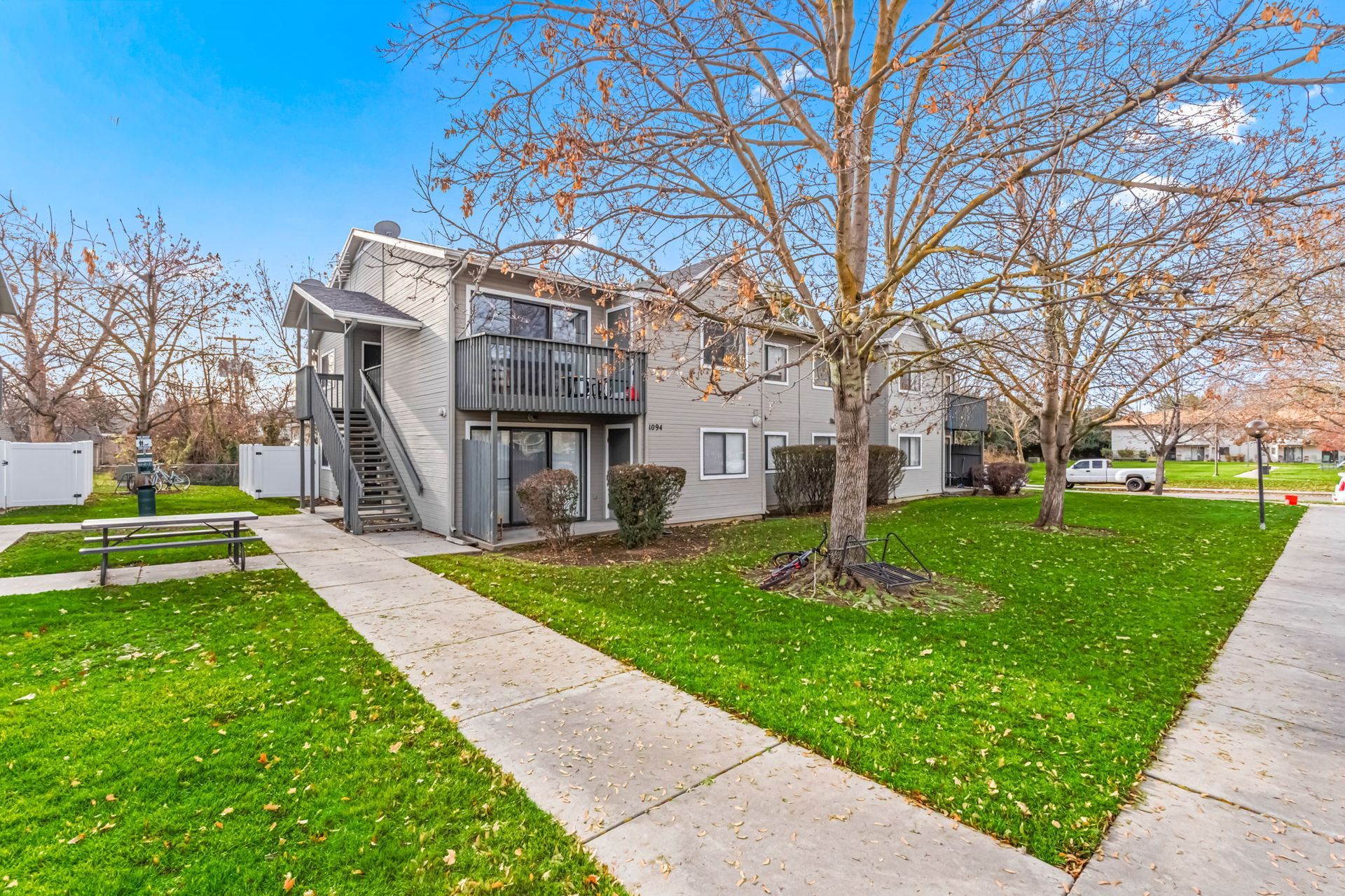 Gray two-story apartment building with staircases, balconies, and a walkway on a grassy lawn.