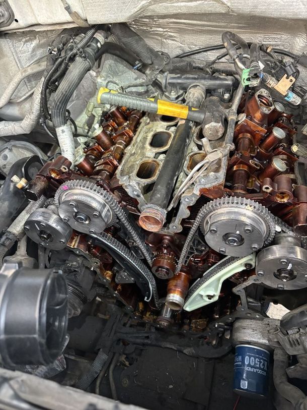Engine bay with disassembled parts, visible camshafts, timing chains, and oil-stained components.