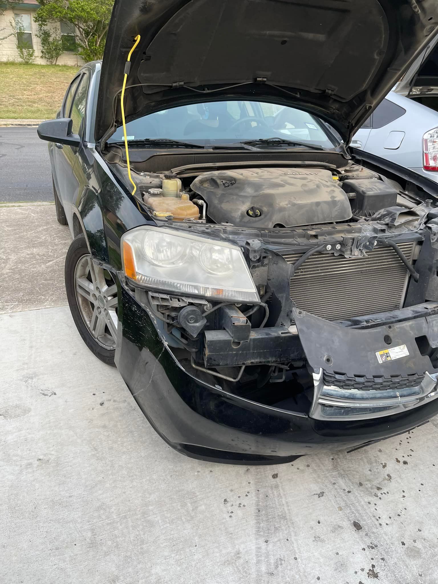 Black car with front-end damage, hood open. Located outdoors on concrete.