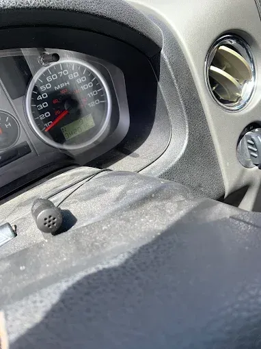 Car dashboard with speedometer, air vent, and earbud on steering wheel.