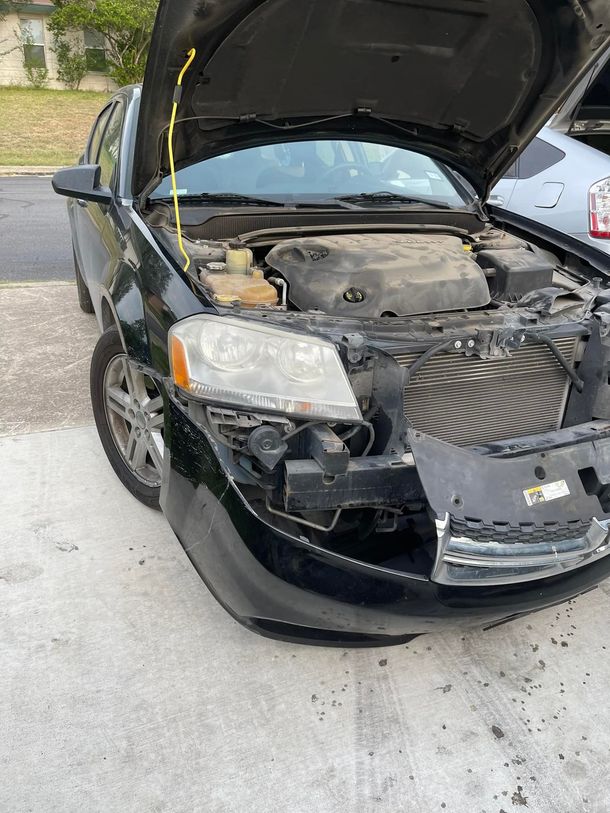 Black car with hood open, front-end damage. Bumper and headlight area appear broken.