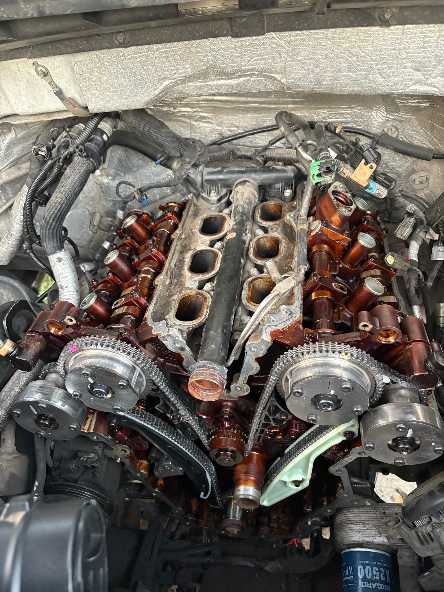 Overhead view of an engine with removed valve covers, showing timing chains, components, and oil.