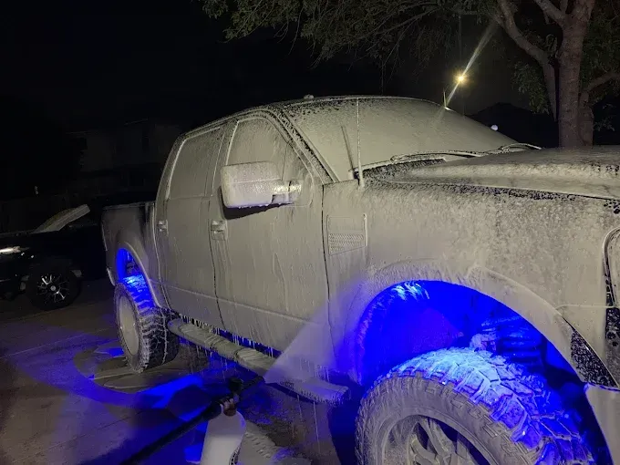 A white truck covered in soap with blue underglow, parked outside at night.