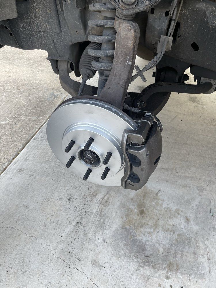 Front wheel assembly of a vehicle with a new brake rotor installed on a concrete surface.