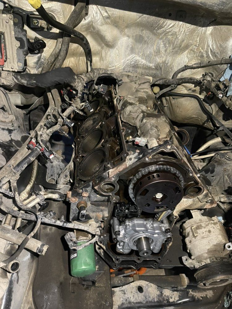 Engine bay with exposed engine components, including timing chain, oil pump, and cylinder head, covered in grease.