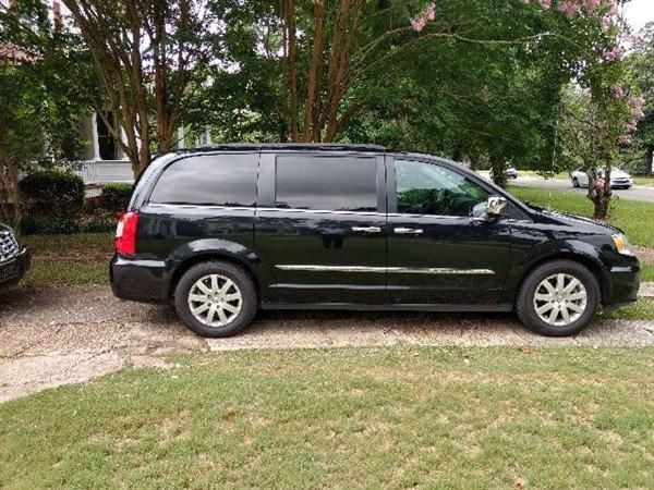 A black minivan is parked in a driveway in front of a house.