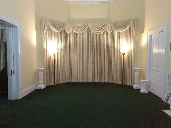 An empty room with green carpet and white curtains.