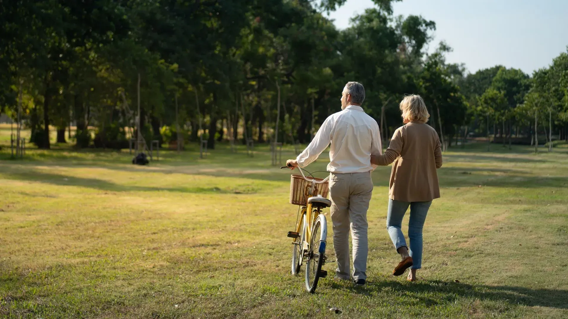 An elderly couple is walking with a bicycle in a park.