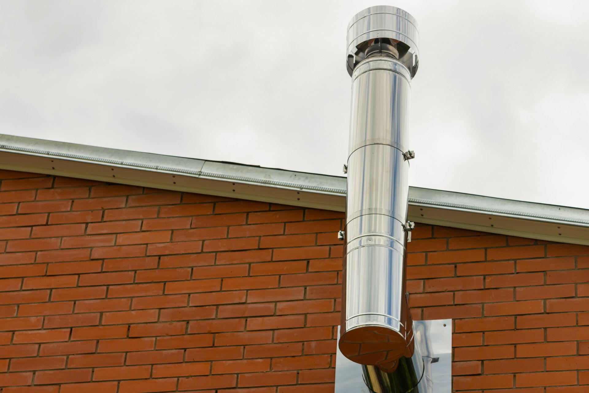 A stainless steel chimney is attached to the side of a brick building.