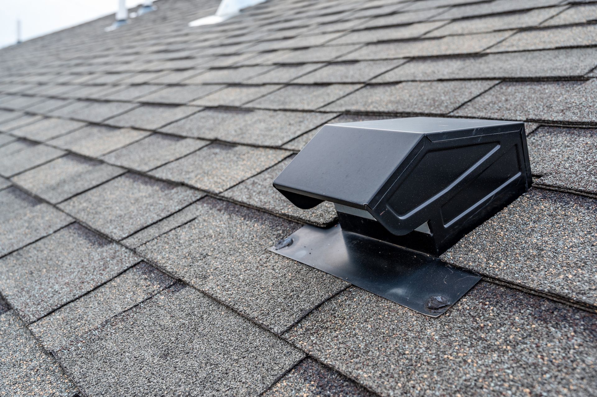 A black roof vent is sitting on top of a shingle roof.