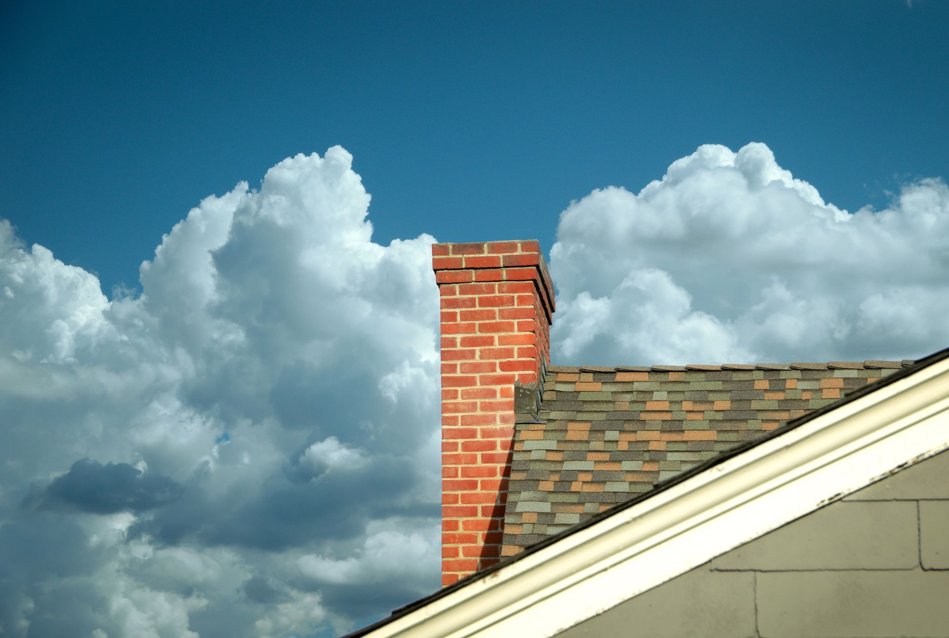 A brick chimney on top of a roof with clouds in the background