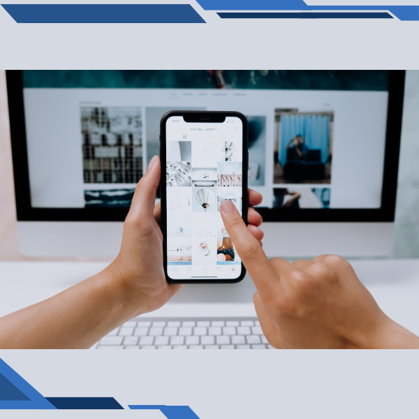 A person is holding a cell phone in front of a computer screen