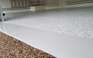 A close up of a white garage floor with gravel underneath it.