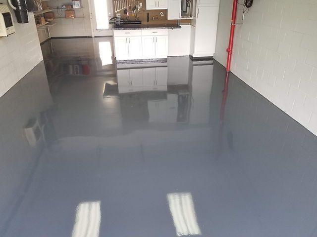 A garage with a gray epoxy floor and white cabinets.