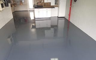 A garage with a gray epoxy floor and white cabinets.