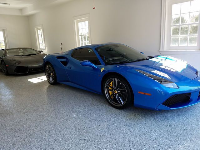 A blue ferrari is parked in a garage next to a black lamborghini