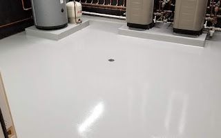 A white floor with a hole in the middle of it in a room with water heaters.