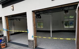 A garage with two garage doors open and a yellow tape covering the floor.