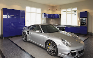 A silver sports car is parked in a garage next to a kitchen.