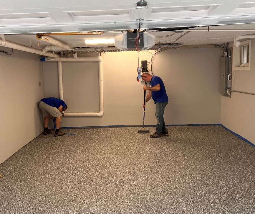 Two men are cleaning a garage floor with a mop.