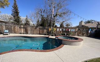 A large swimming pool with a hot tub in the backyard of a house.