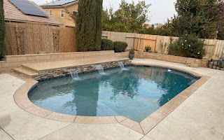 A large swimming pool with a waterfall in the backyard of a house.