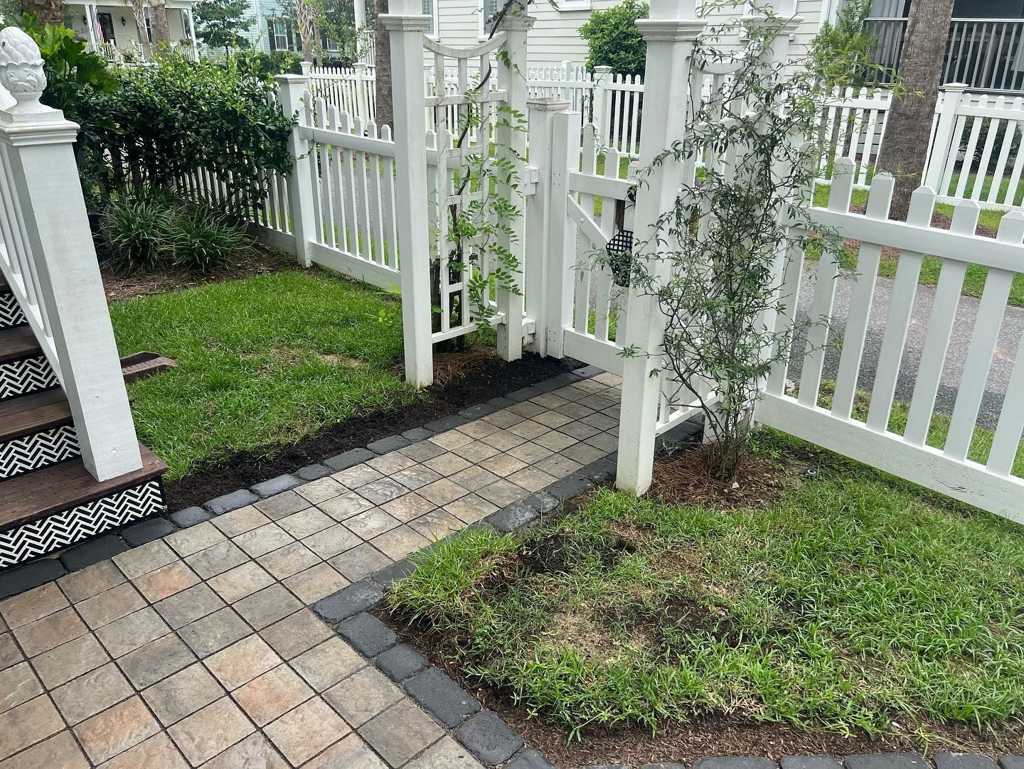 A white picket fence surrounds a brick walkway in a yard - Mount Pleasant, SC - C&B Landscape LLC