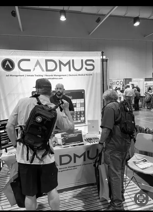 People browsing a CADMUS booth at a trade show, with product displays and banners.