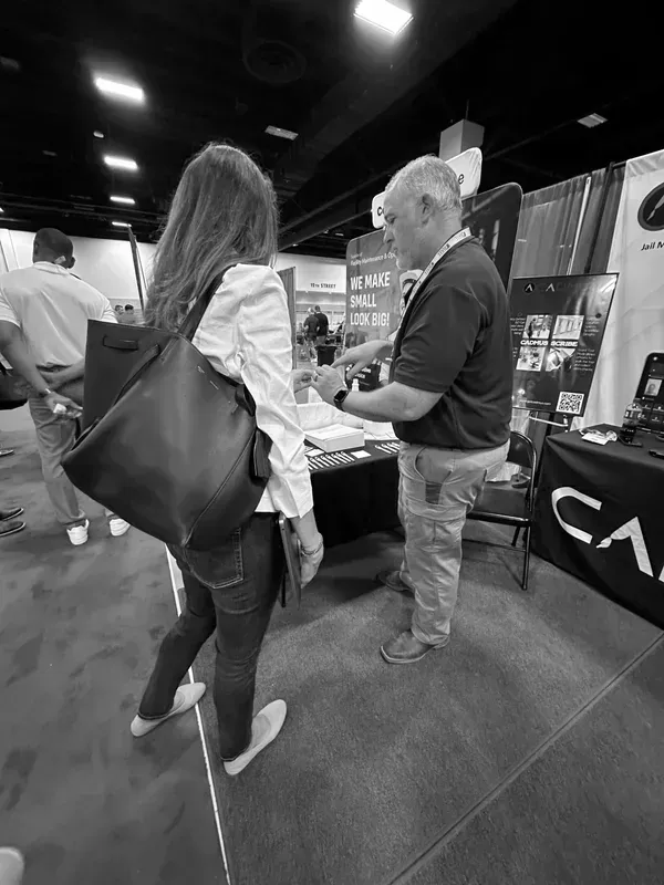 Two people talking at an indoor trade show booth, with banners and a Canon display in the background.