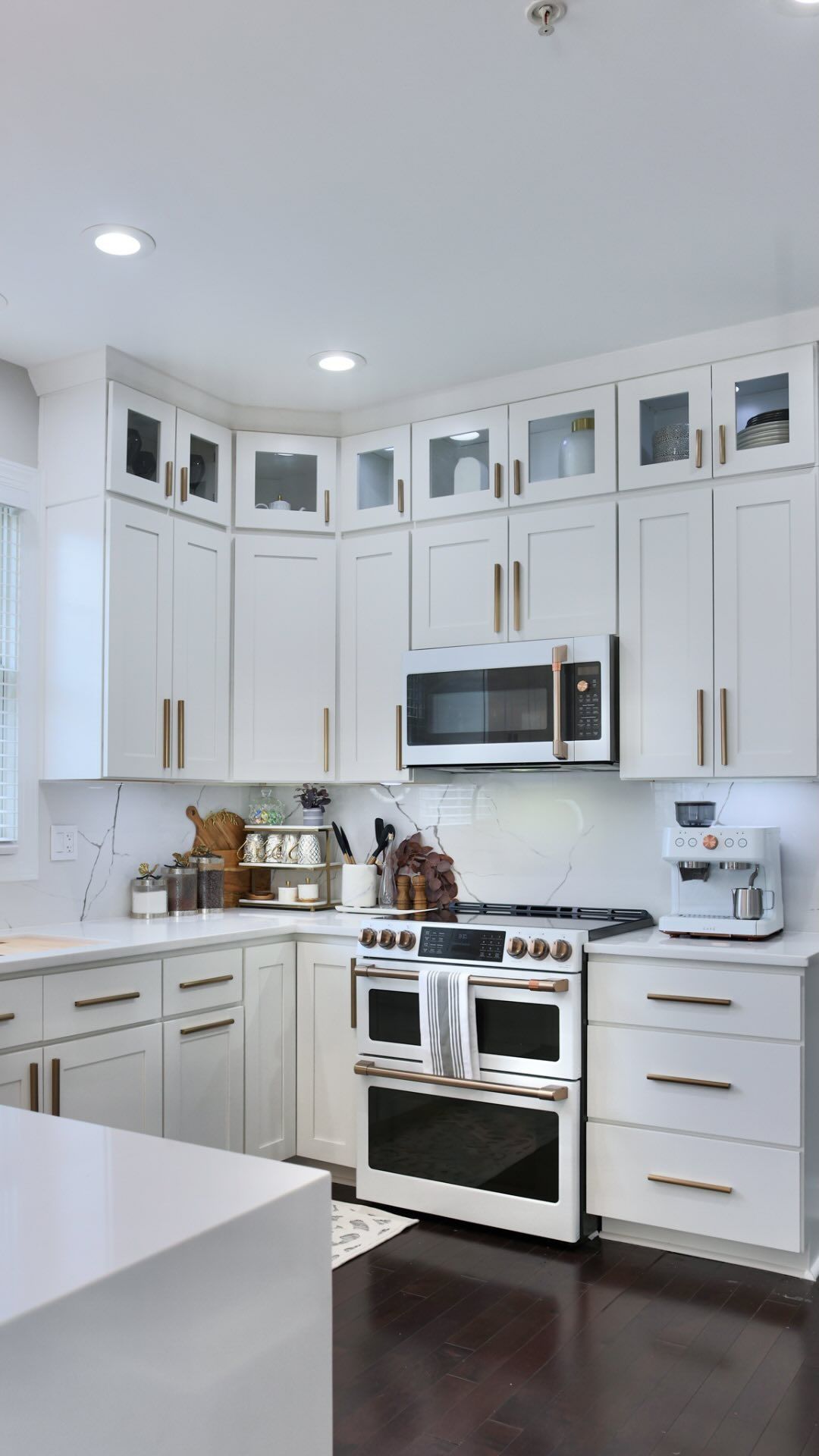 A kitchen with white cabinets , a stove , a microwave , and a coffee maker.