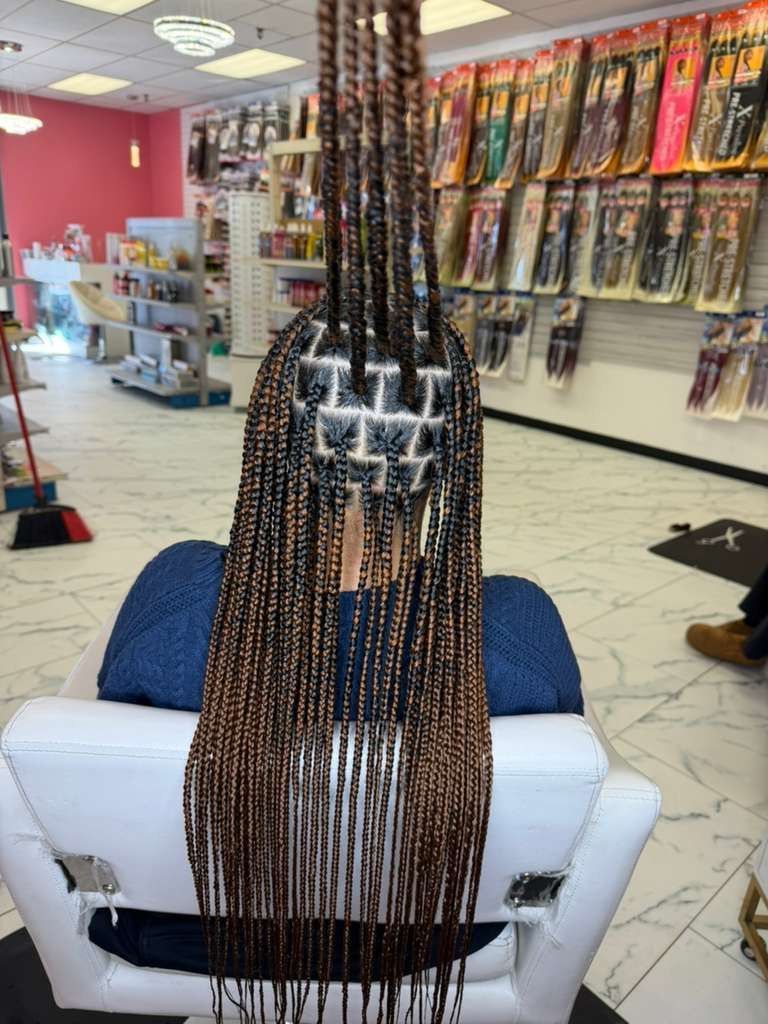 Person getting long box braids in a beauty supply store. Braids are a mix of brown and black.