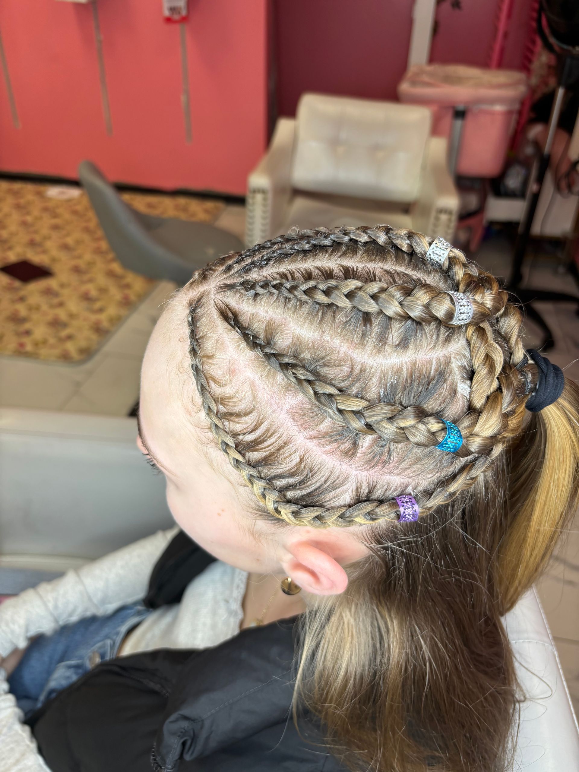 Close-up of blonde braids on the scalp, pulled back into a ponytail with small colorful clips.