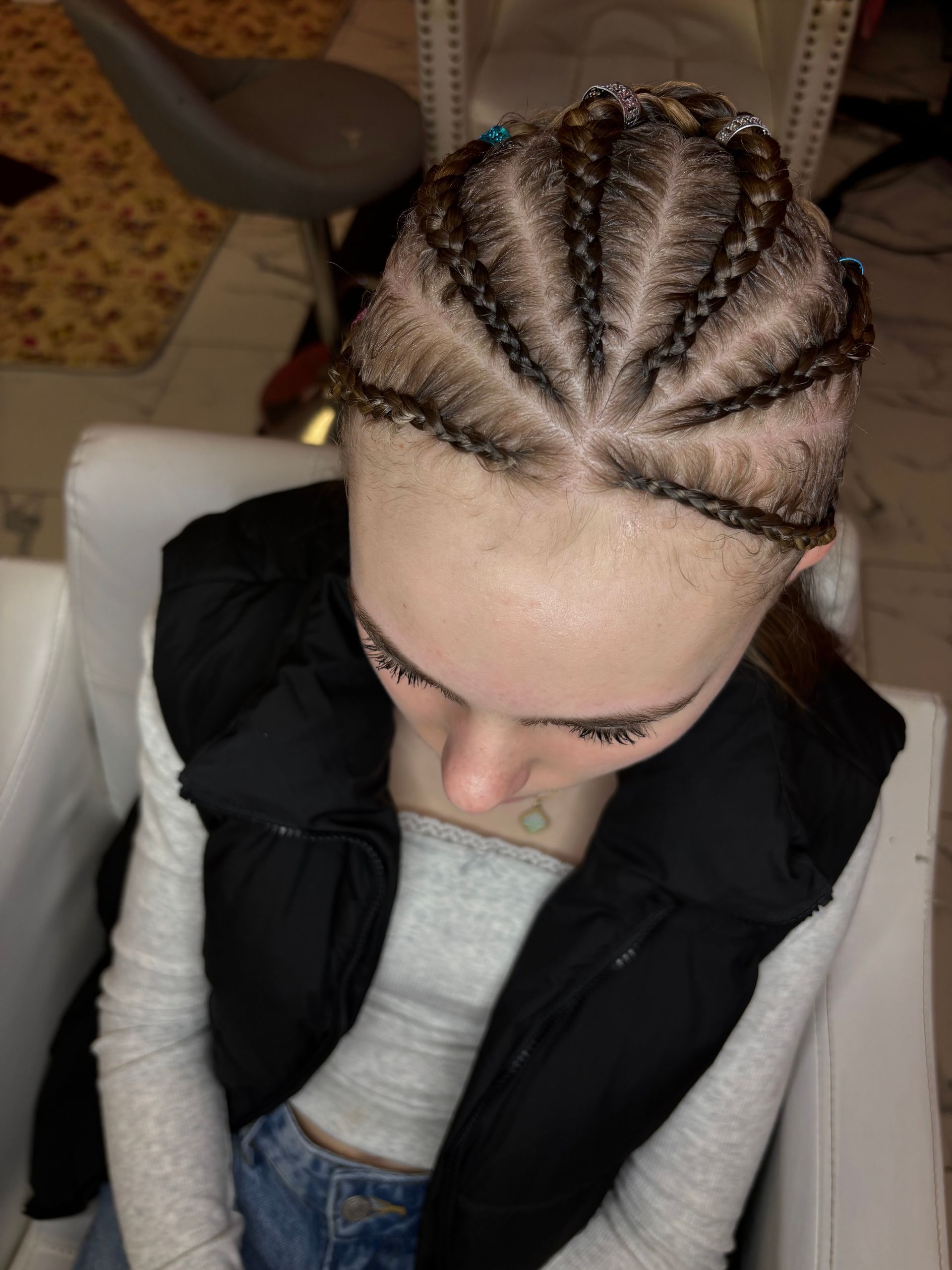 Person with braided hairstyle, wearing a white top and black vest.