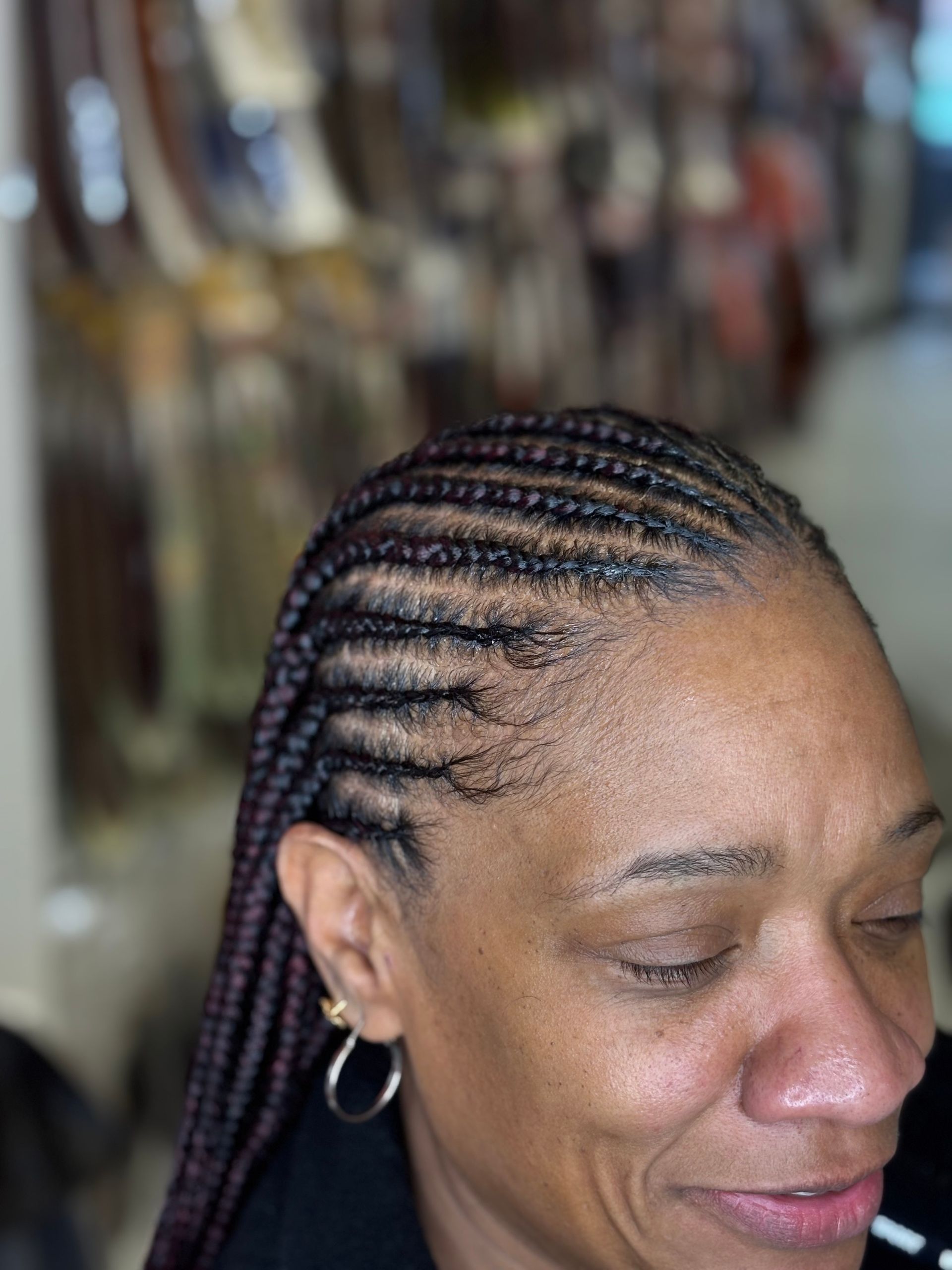 Woman with braided hair, eyes closed, wearing hoop earrings, in front of a blurred background.