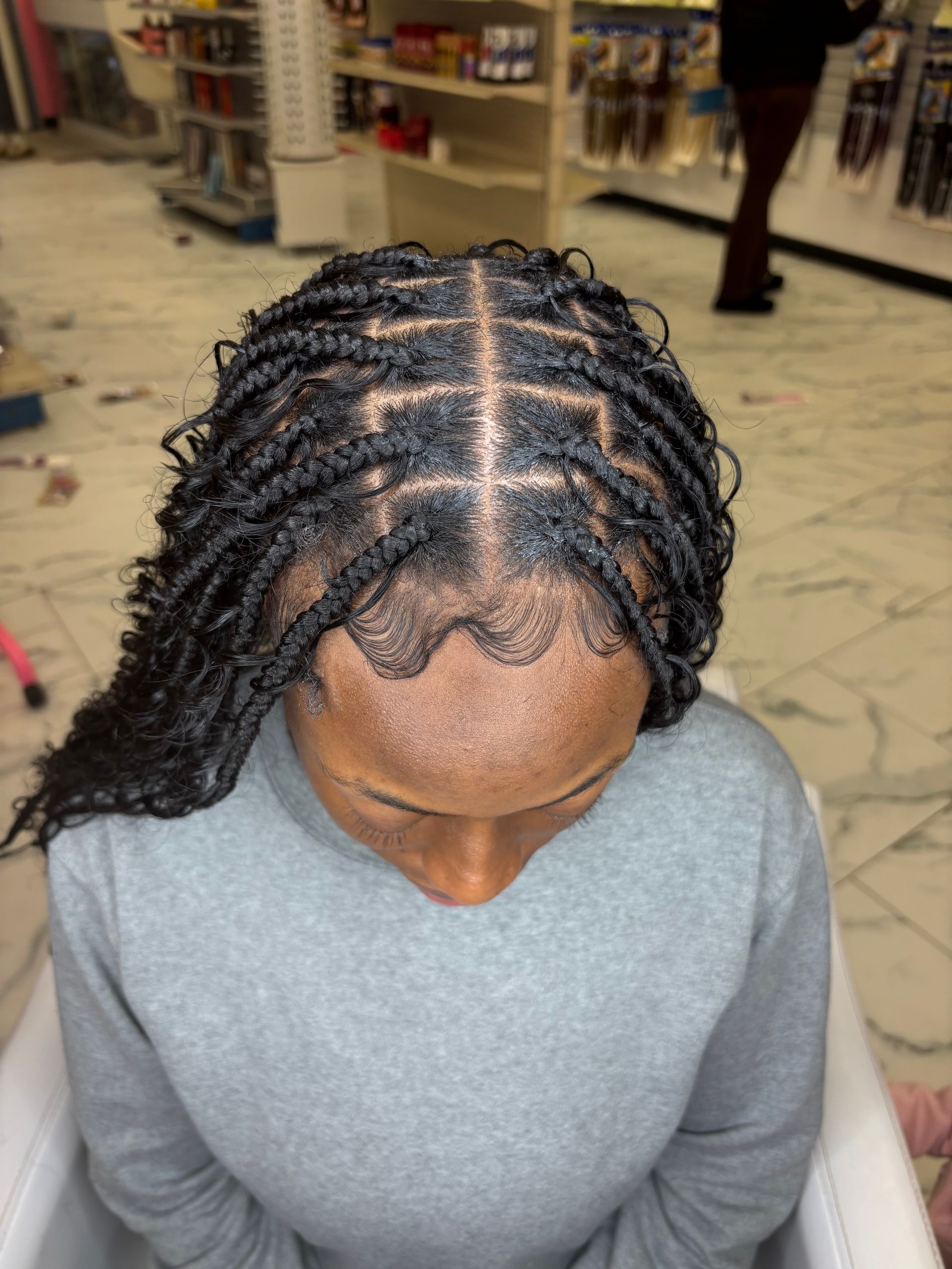 Close-up of a person's head with neatly styled black faux locs. Light gray shirt and salon setting in the background.