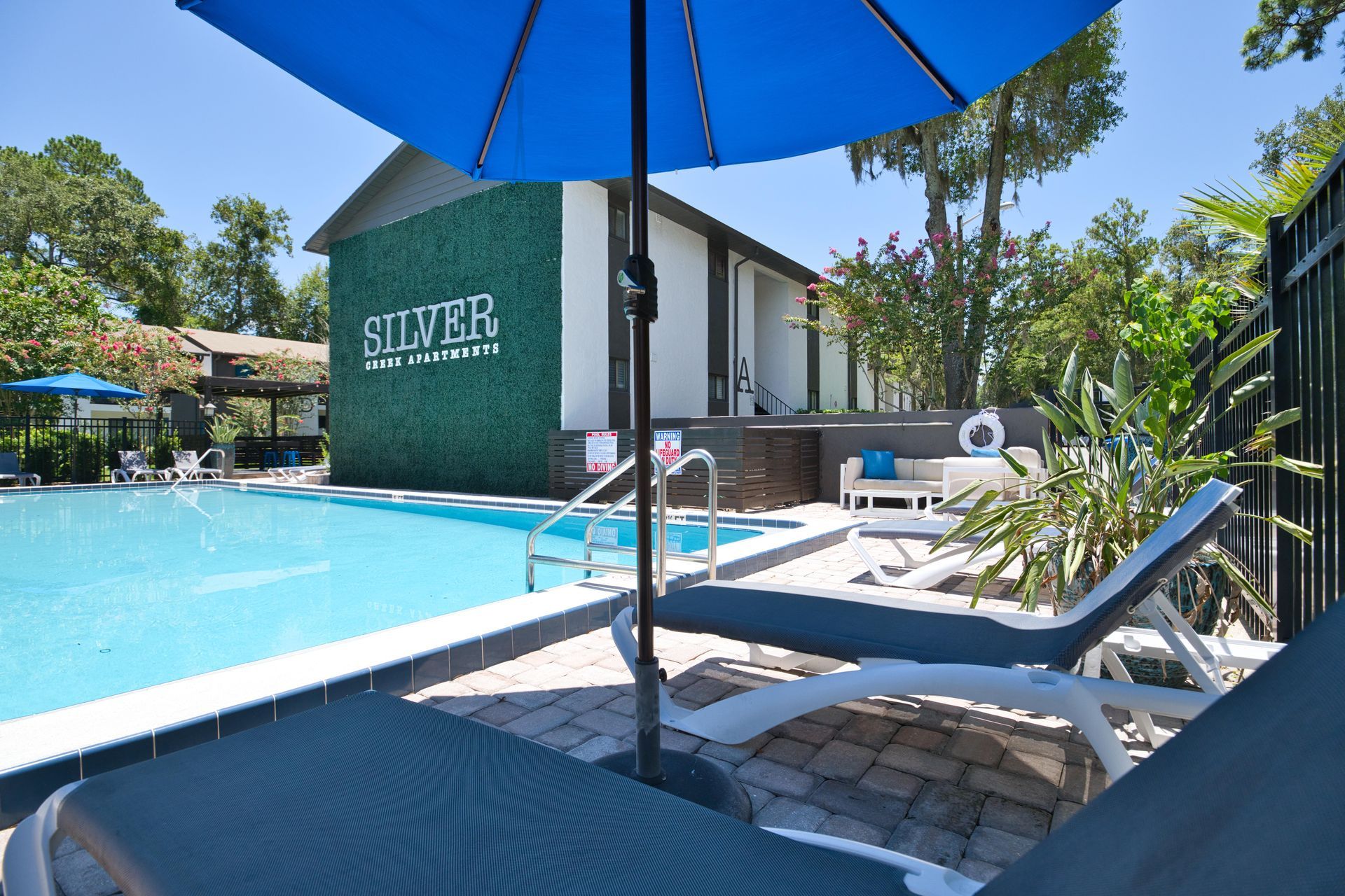 A swimming pool with a blue umbrella in front of a building that says silver