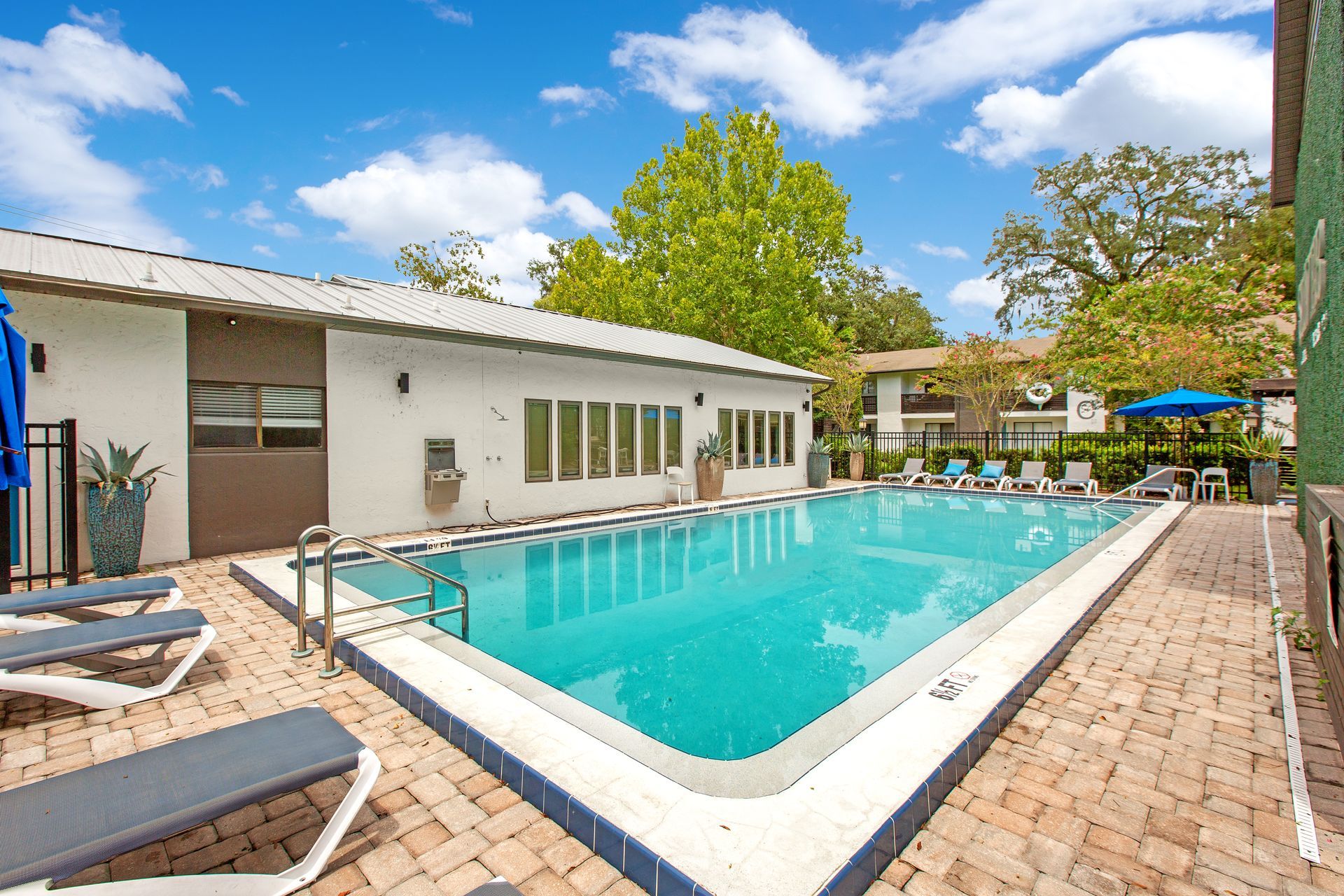 A large swimming pool is surrounded by chairs and umbrellas in front of a building.