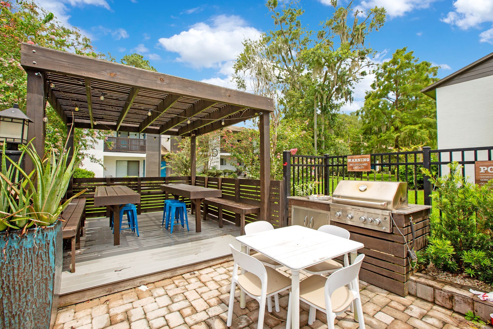 A patio with tables and chairs under a pergola and a grill.
