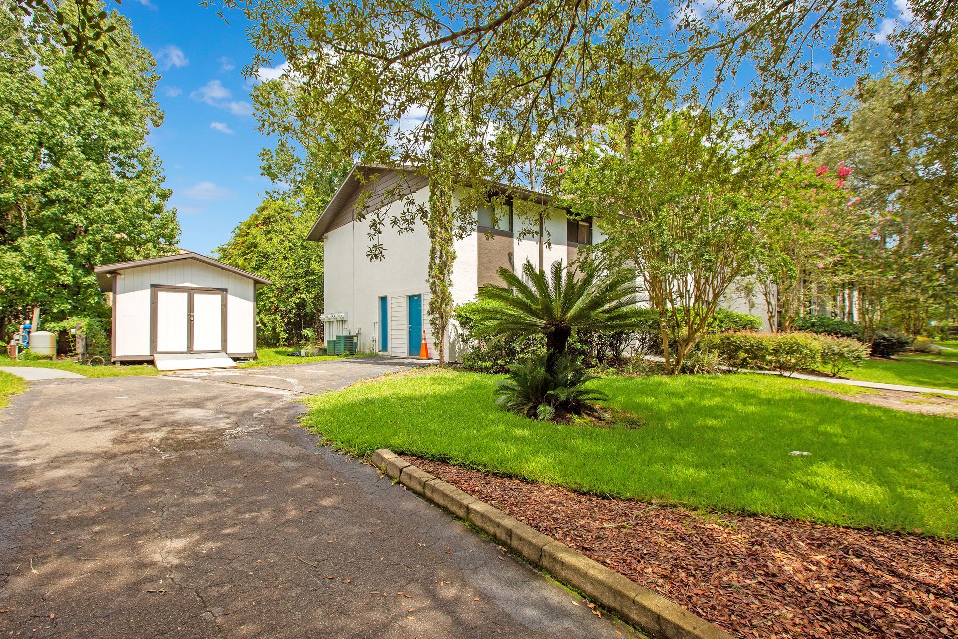 A white house with a driveway leading to it is surrounded by trees and grass.