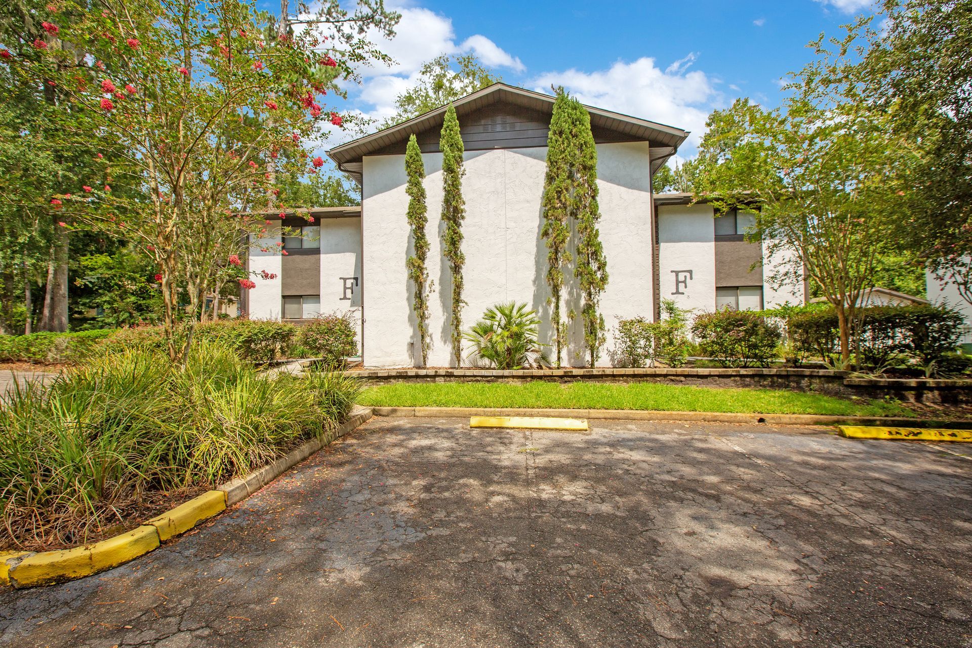 A large white apartment building with a parking lot in front of it.