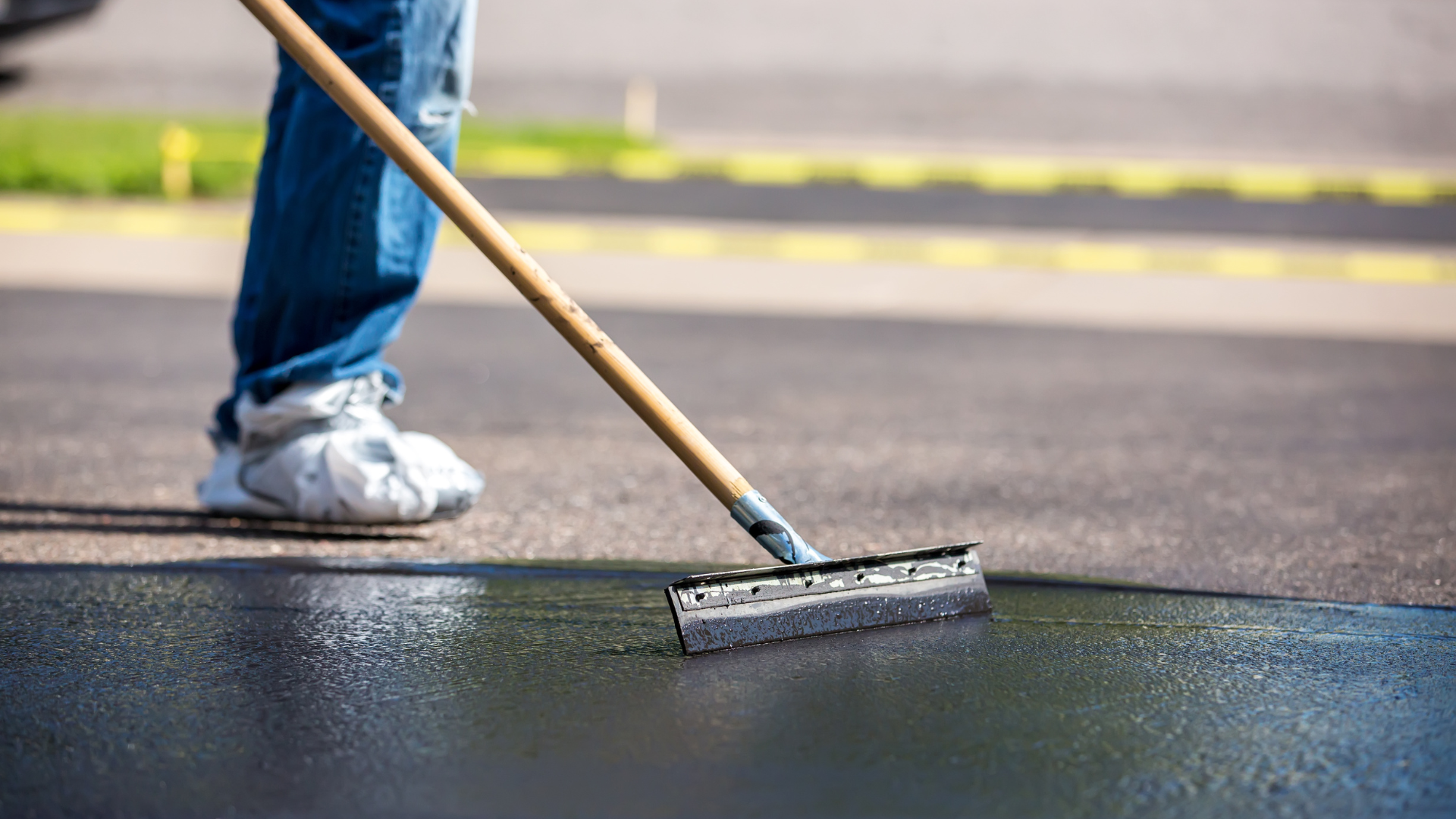 A person is using a broom to spread asphalt on the ground.