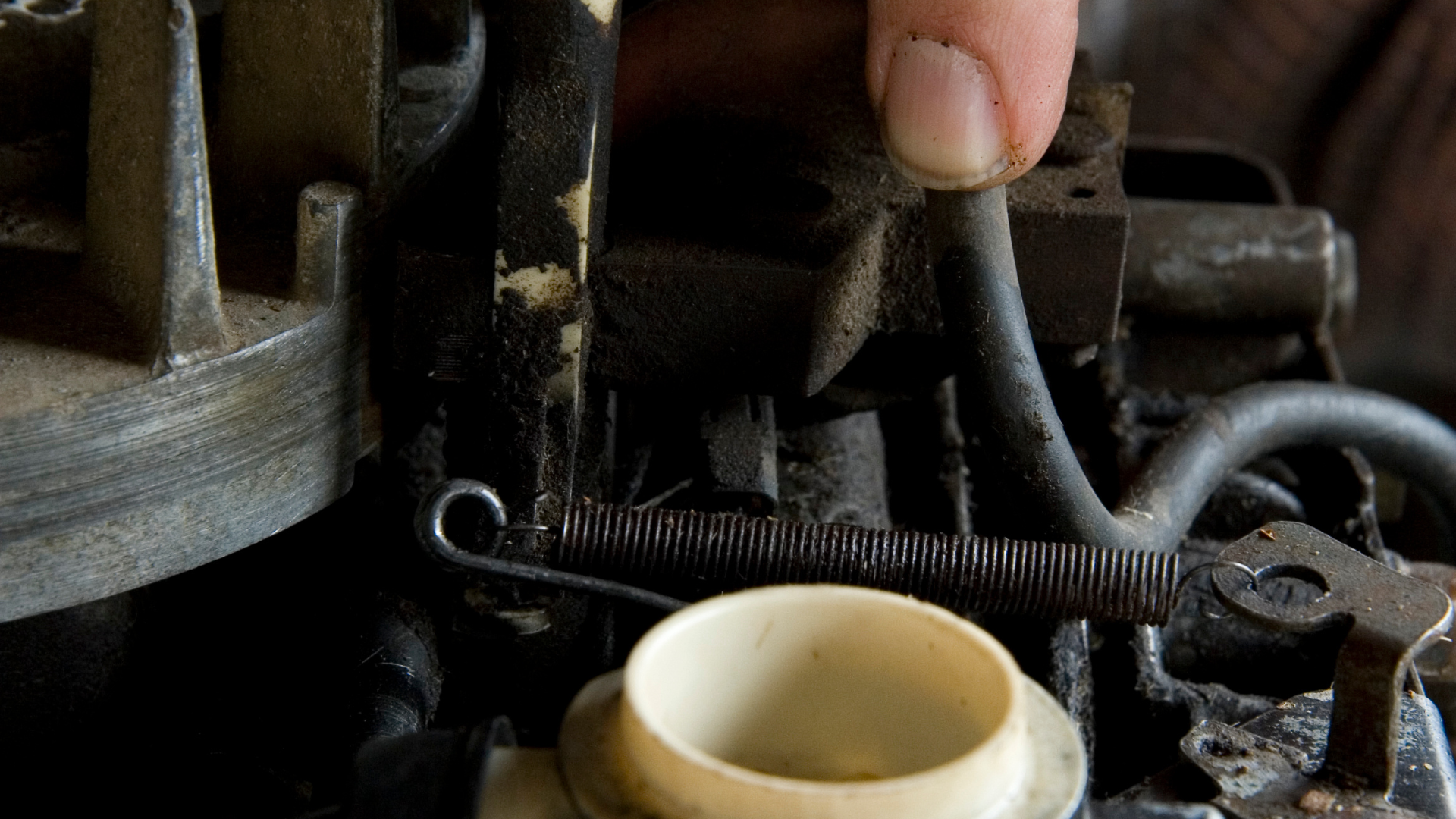 A person is fixing a carburetor on a lawn mower.