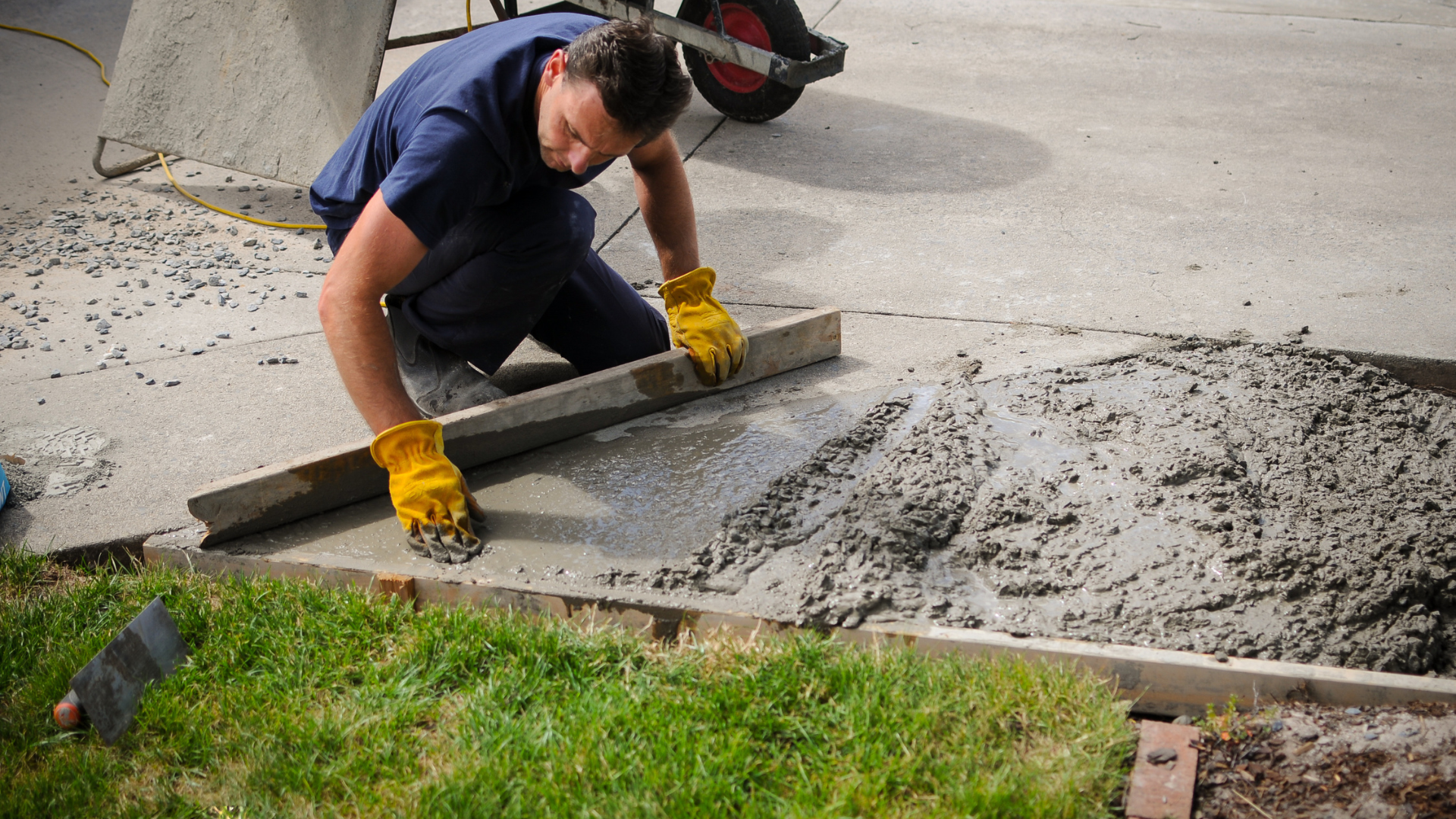 A man wearing yellow gloves is working on a concrete driveway.