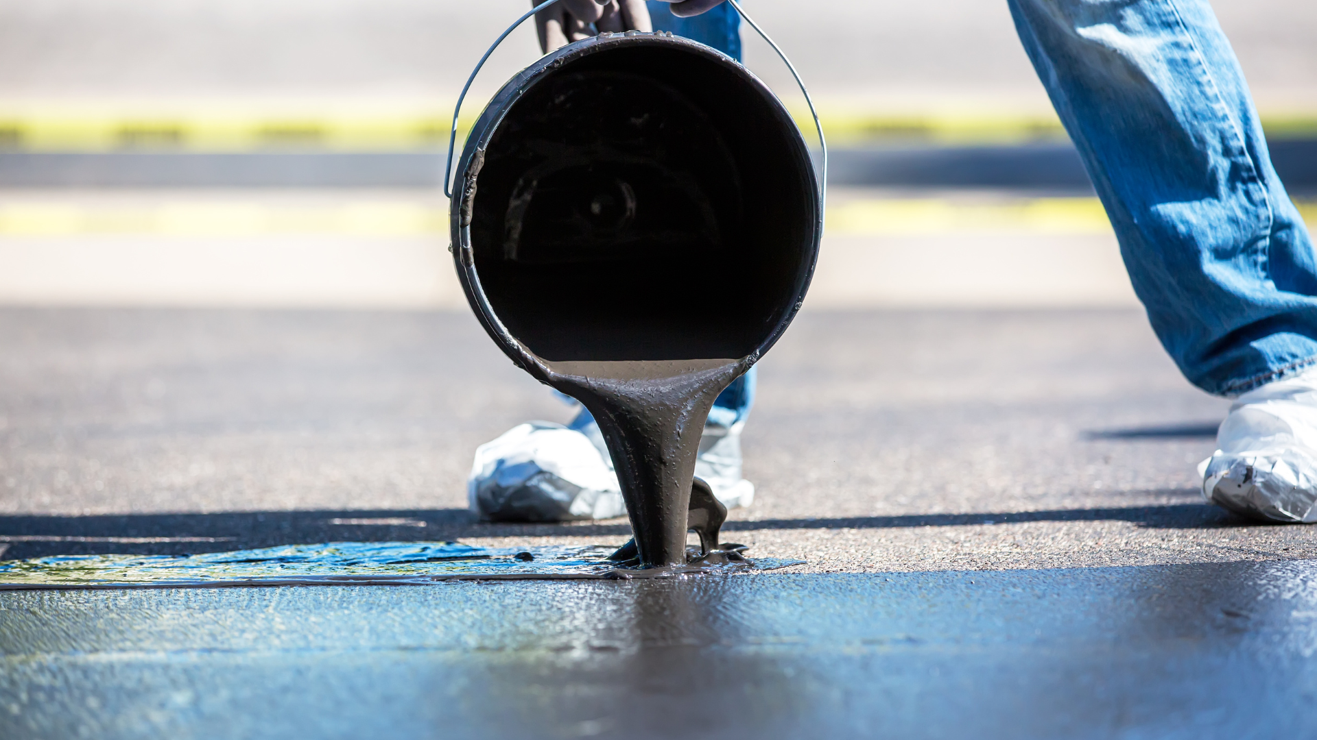 A person is pouring asphalt from a bucket onto the ground.