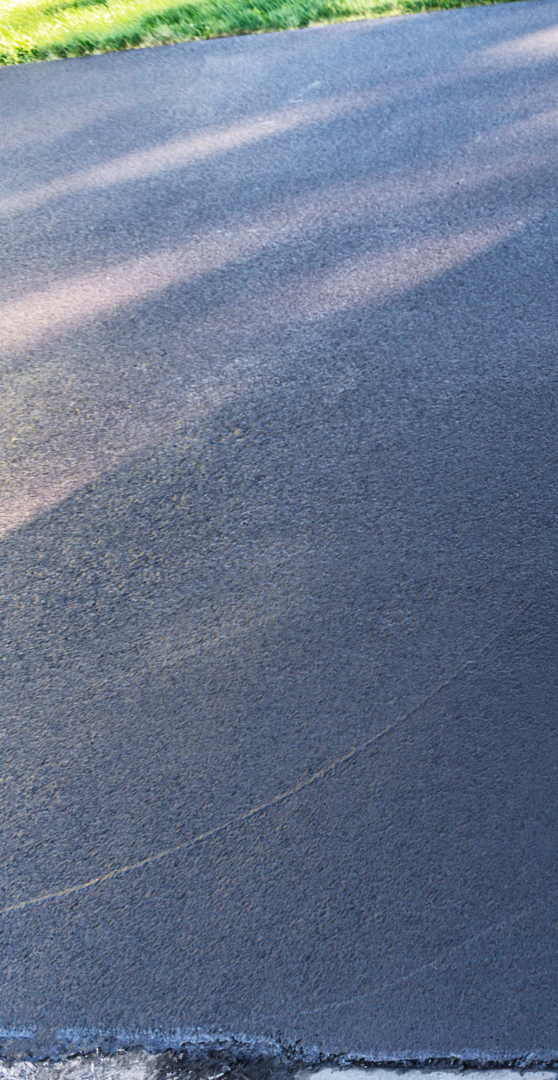 A close up of a black asphalt road with trees in the background.