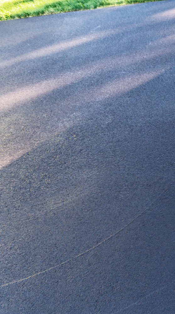 A close up of a black asphalt road with trees in the background.