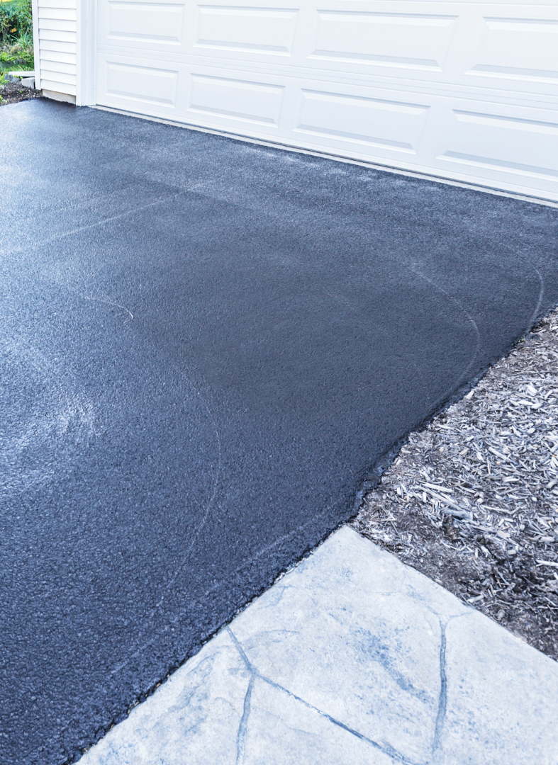 A black asphalt driveway next to a white garage door.