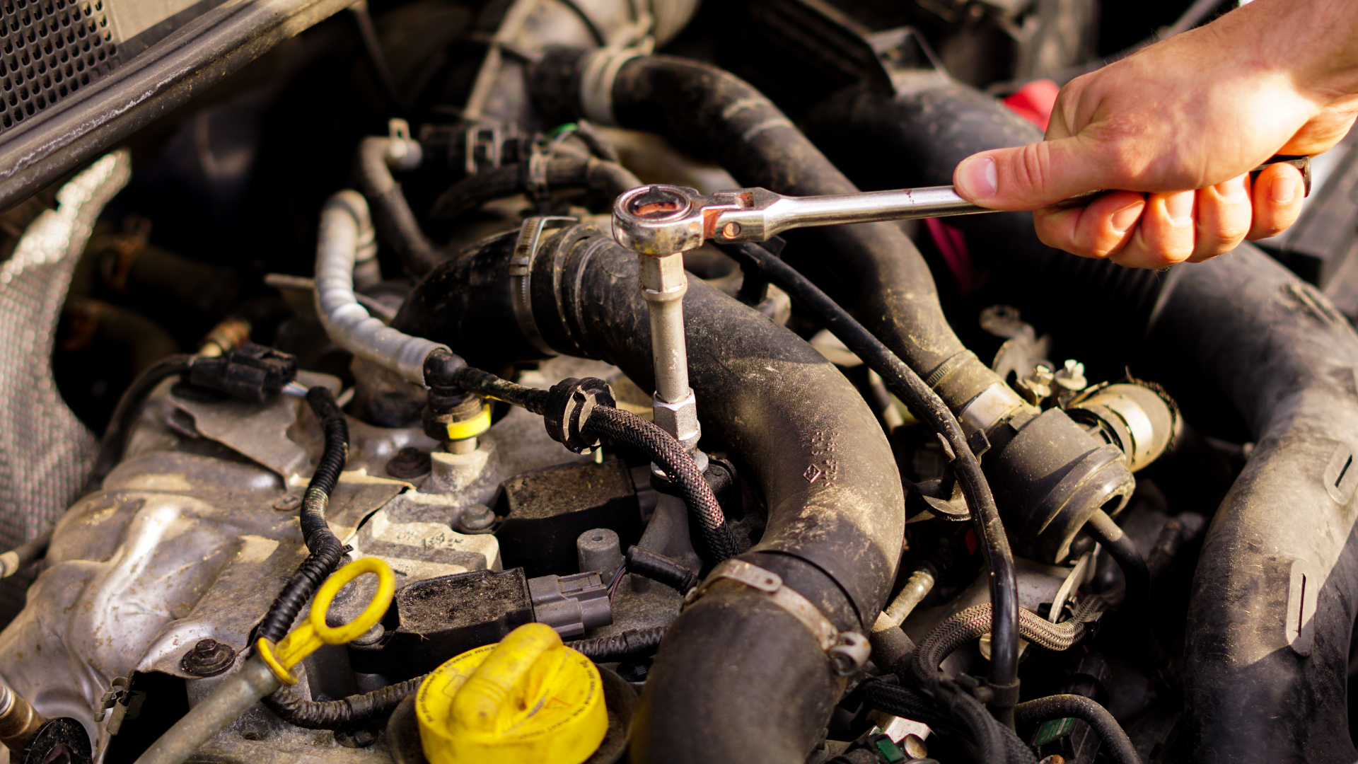 A person is working on a car engine with a wrench.