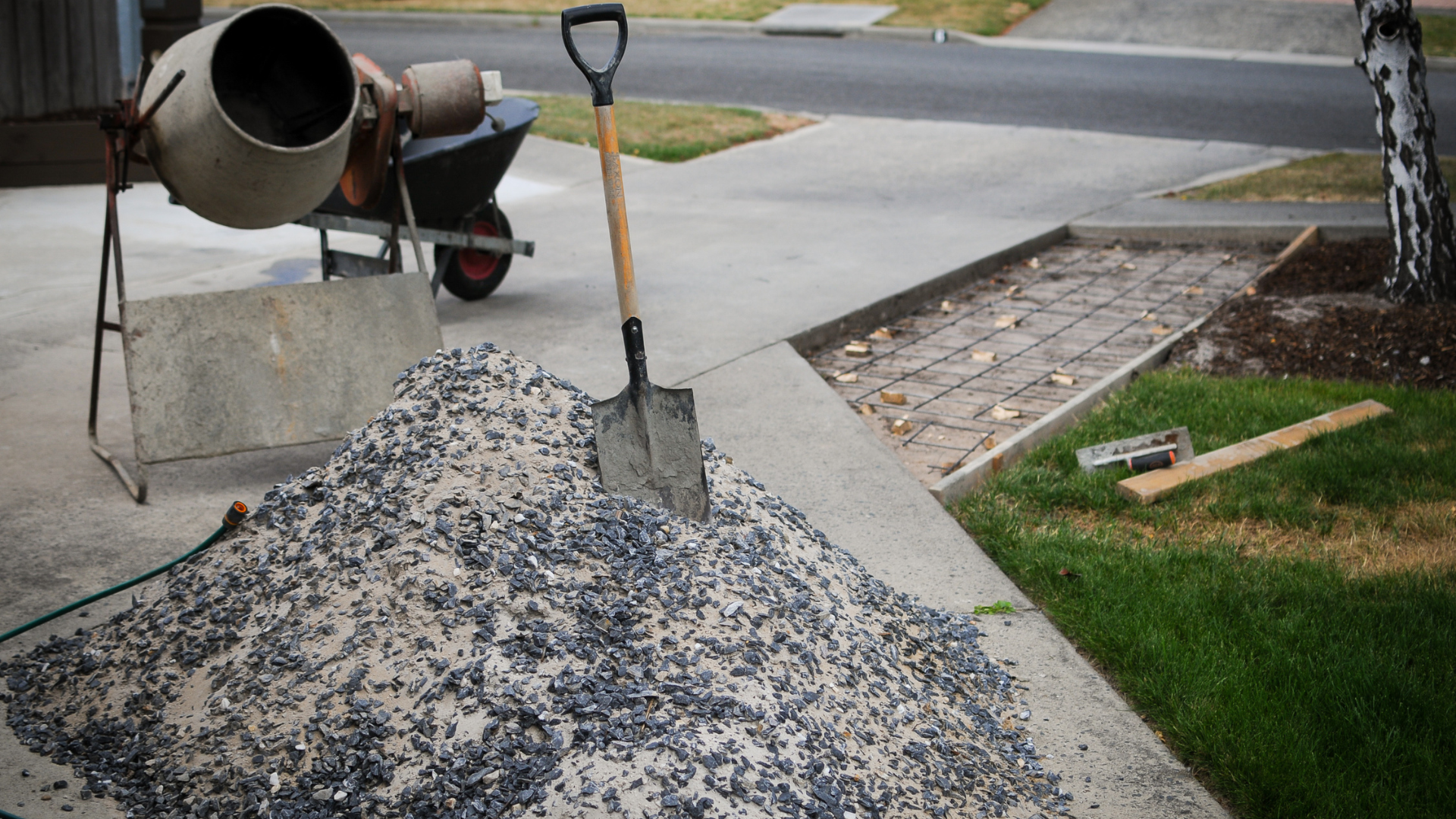 A shovel is sitting on top of a pile of gravel next to a cement mixer.