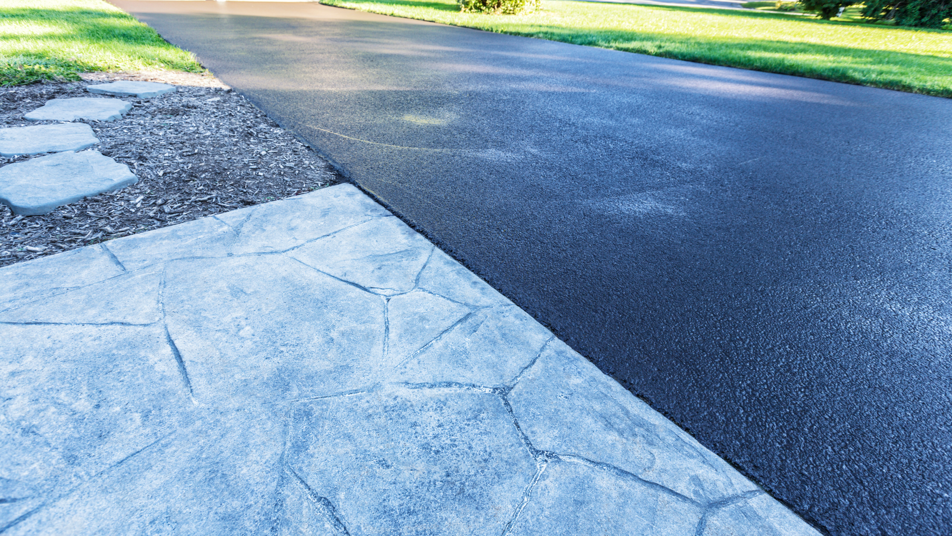 A black asphalt driveway with a stone walkway on the side of it.